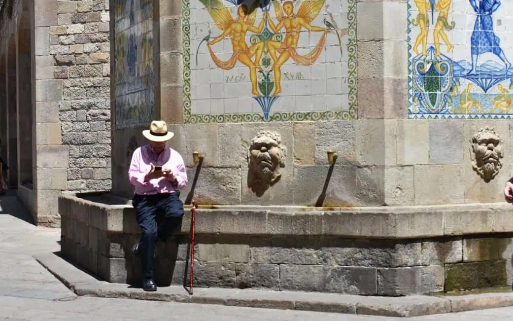 a man checking his phone near a fountain in the gothic quarter of barcelona spain