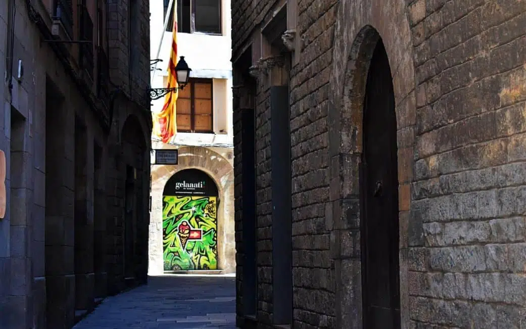 a dark alleyway in the gothic quarter leading to some street art at the back of a gelato shop in barcelona spain