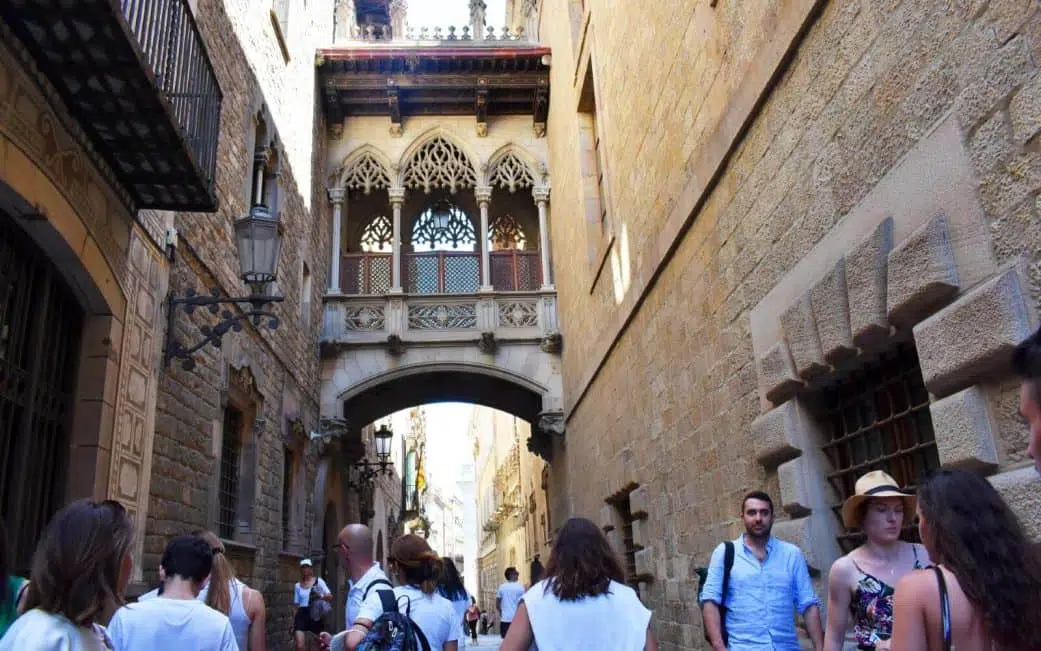 tourists walking under the pont del bisbe in the barcelona gothic quarter