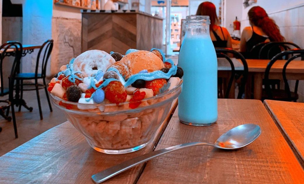 a indoor table with a silver spoon a bowl of breakfast cereal and a bottle of blue milk at el flako barcelona