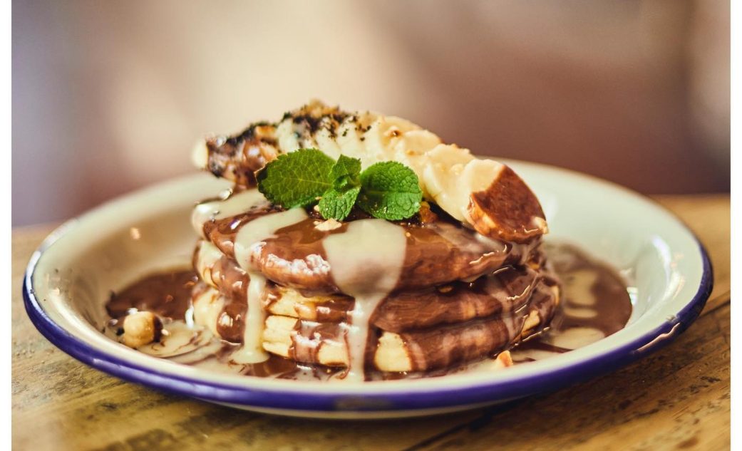 a stack of pancakes with chocolate and banana topping and mint leaves at granja petitbo in barcelona