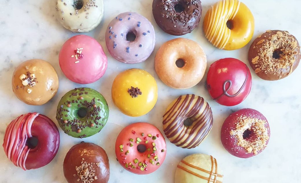 a marble table full of colorful donuts of various flavours at la donuteria in barcelona